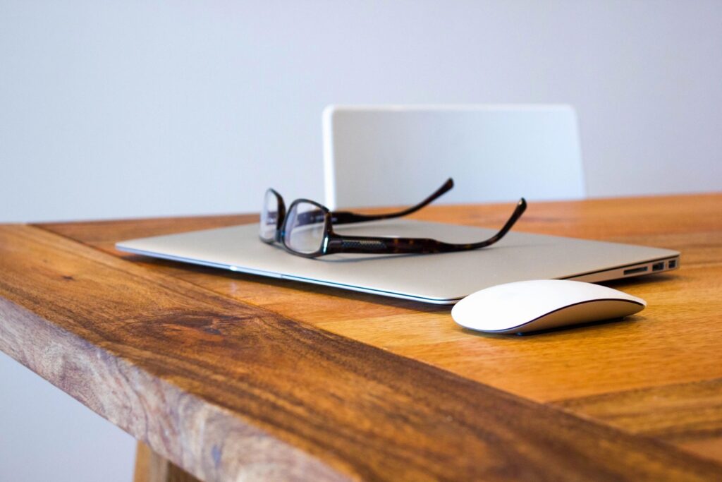 Re-opening the workplace header. Features glasses on a laptop next to a mouse on a wooden table.